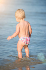Baby playing on the sandy beach and in sea water. Cute little kid with toys on sand tropical beach. Ocean coast.