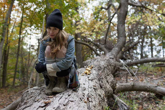 Portrait of young woman sitting on tree trunk in forest
