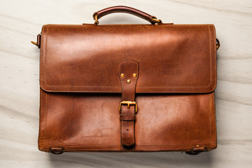 Brown Vintage leather briefcase with strap and brass buckle on wood background,