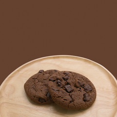 Chocolate cookies with chocolate chip on round wooden plate isolated on brown background with copy space