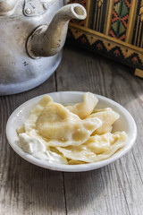 Traditional Ukrainian and Russian cuisine , dumplings called varenyky of dough with cottage cheese and sour cream in a clay plate with national attributes on a wooden background