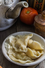 Traditional Ukrainian and Russian cuisine , dumplings called varenyky of dough with cottage cheese and sour cream in a clay plate with national attributes on a wooden background