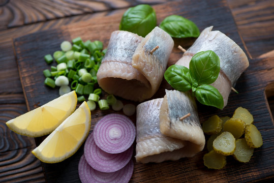 Herring rollmops with red and green onion, gherkins and lemon