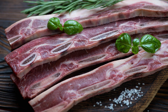 Close-up of uncooked beef ribs with rosemary, basil and sea salt