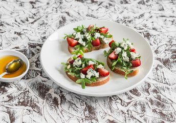 Sandwiches with strawberries, arugula and blue cheese on a white ceramic plate, on a light background. Delicious snack, breakfast or  appetizer with wine