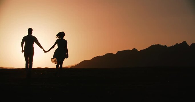 couple silhouette running forward holding hands with the sunset Golden hour, the sun a warm color, slow motion