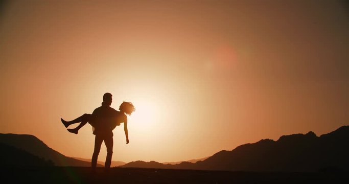 Romantic young couple silhouette. the guy holding the hands of the girl to whirl together ,sunset, flare, love story, slow motion