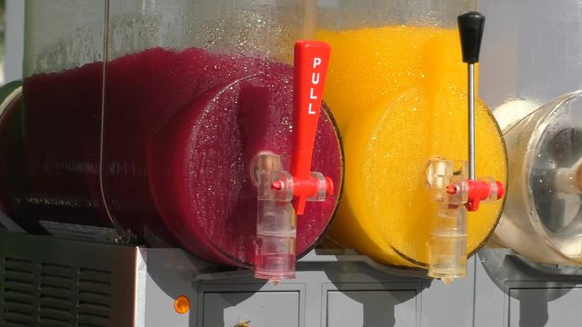 Red and yellow slushies stirring in the commercial slush machine or maker, two wasps looking for sweet food
