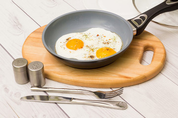 Frying pan with cooked two eggs and spices