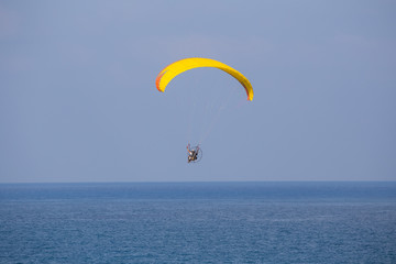 A yellow-orange propelled paraglider in a low flight over the sea