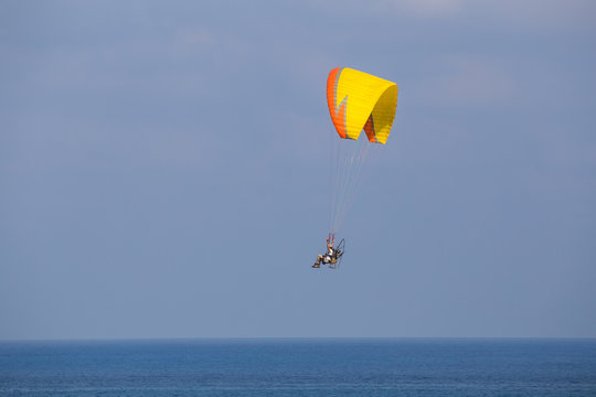 A yellow-orange propelled paraglider in a low flight over the sea