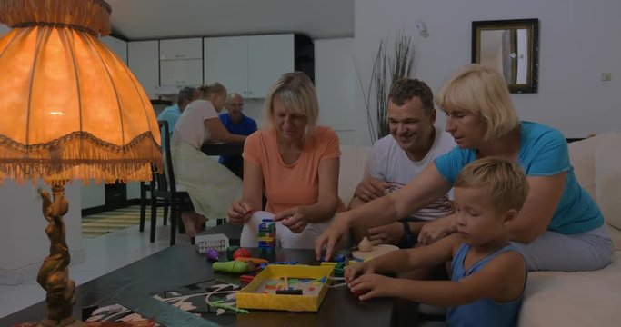 Little boy spending home leisure with father and two grandmothers. They playing with construction kits in the living room