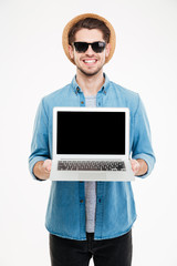 Smiling young man standing and holding blank screen laptop