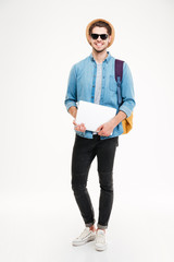 Smiling young man holding backpack and laptop