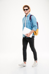 Cheerful young man with backpack walking and holding laptop