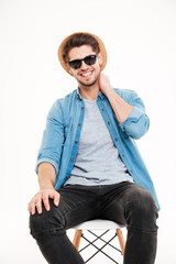 Happy young man in hat and sunglasses sitting on chair