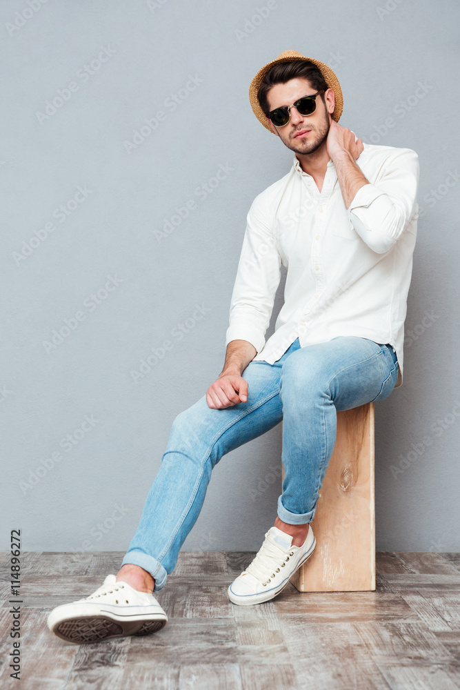 Wall mural Relaxed young man in white shirt, jeans, hat and sunglasses