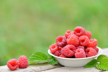 Fresh red raspberries on plate on blurred natural background