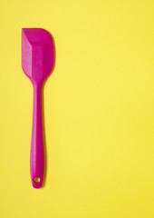 A pink baking spatula on a yellow background