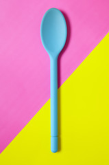 A blue silicone cooking spoon on a pink and yellow background