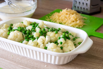 Cooking cauliflower and peas gratin in a baking tin on white wooden background