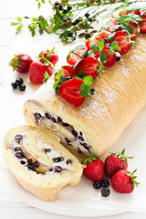 Biscuit roll with mascarpone cream and blueberries decorated strawberries, blueberries and mint leaves on white wooden background