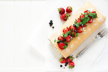 Biscuit roll with mascarpone cream and blueberries decorated strawberries, blueberries and mint leaves on white wooden background