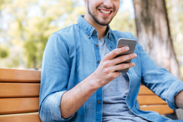 Cropped image of a smiling man with smartphone sitting outdoors