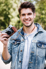 Close-up portrait of a handsome guy holding camera outdoors