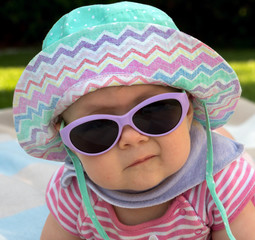 Baby mit Sonnenhut und Sonnenbrille im Garten
