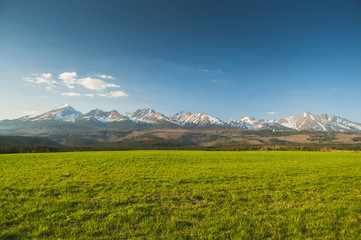 High tops. A long strip of high mountains. In the foreground of the green grass
