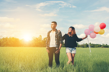 Young Couple in love with balloons in hands in the green grass b