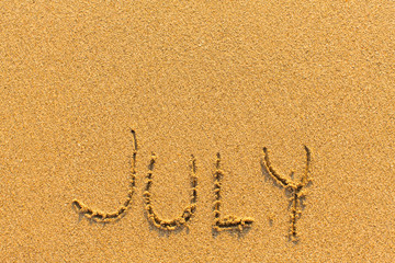 JULY drawn by hand on a golden sandy sea beach.