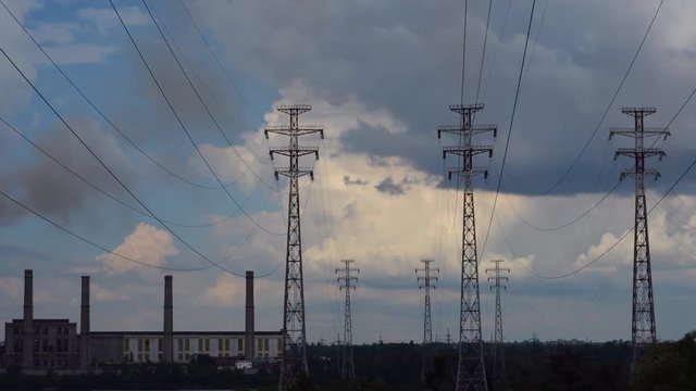 Electrical pylons with timelapse clouds. On the left are visible pipe thermal power plant. Electricity pylon with stormy sky on the background. 4K