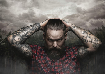 Brutal bearded male with tattooed arm looks down.