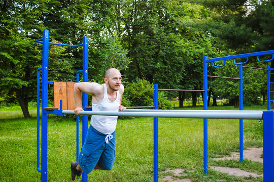 Fitness, sport, exercising, training and lifestyle concept. Young man doing triceps dip on parallel bars, outdoors.