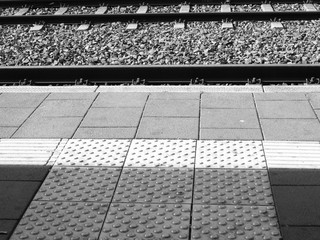 Bahnsteigkante mit taktilem Leitsystem und Bahngleisen im Schotterbett bei Sonnenschein im Bahnhof...