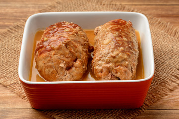 Roasted meat roulades with sauce on wooden background.