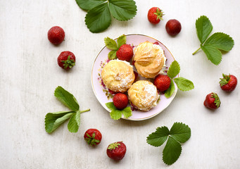 Cream puffs or profiterole filled with whipped cream served with strawberries on a stone grey board...