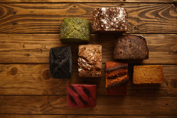 Many mixed alternative baked breads presented as samples for sale on rustic wooden table in professional bakery: pistachio,beetroot,tomatoes,lavender,sea salt, coal,sweet potato