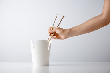 Woman hand uses chopsticks to pick up tasty noodles from takeaway blank box isolated on white...