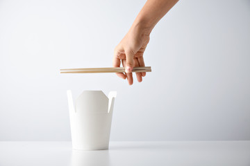 Woman hand holds chopsticks above opened blank takeway box with tasty noodles isolated on white Retail set presentation mockup