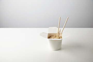 Tasty noodles with soy sause and spices inside blank takeaway paper wok box isolated on white with chopsticks inside