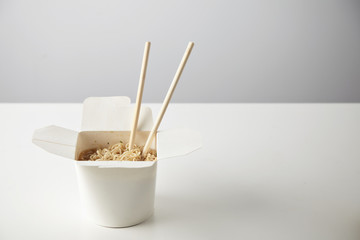 Tasty noodles with soy sause and spices inside blank takeaway paper box with chopsticks inside isolated on white