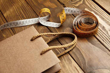 Brown takeaway bag from thic recycled craft paper on rustic wooden table near vintage tailoring meter close view mockup