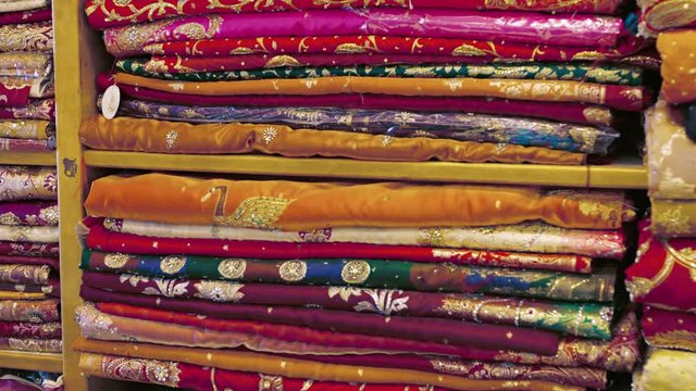 Row upon row of colorful, intricately decorated, Indian style clothing, neatly folded and stacked on shelves in a streetside shop.