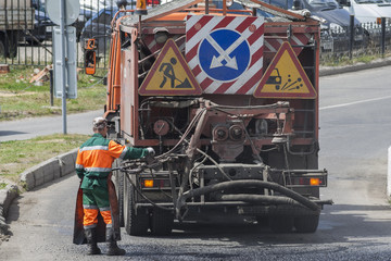 Road worker carries out repairs to the road, using a special truck fills holes with bitumen