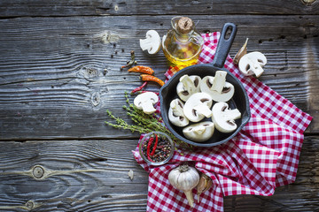 Kitchen still-life with mushrooms in a black cast iron skillet, new potatoes, garden herbs, onions and garlic on  wooden background