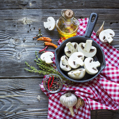 Kitchen still-life with mushrooms in a black cast iron skillet, new potatoes, garden herbs, onions and garlic on wooden background