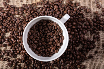 White cup with coffee seeds on jute bag